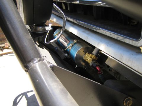 1990 Ford Bronco - blue anodized cylinder with a braided line and brass fitting is bolted within a tubular frame structure beneath a vehicle.