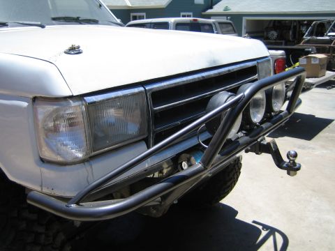 1990 Ford Bronco - front of a white SUV with a black tubular bumper holding two round driving lights and a trailer ball, parked in a driveway.