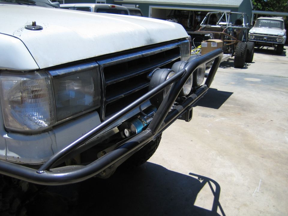 Front corner of a white SUV with tube bumper and project vehicles behind