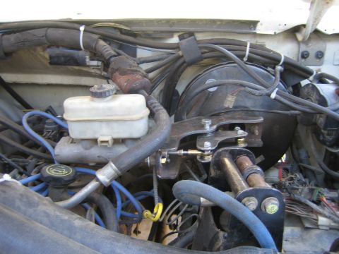 1990 Ford Bronco - Under-hood view showing the brake master cylinder reservoir, round vacuum booster, blue plug wires and a metal bracket secured with bolts.