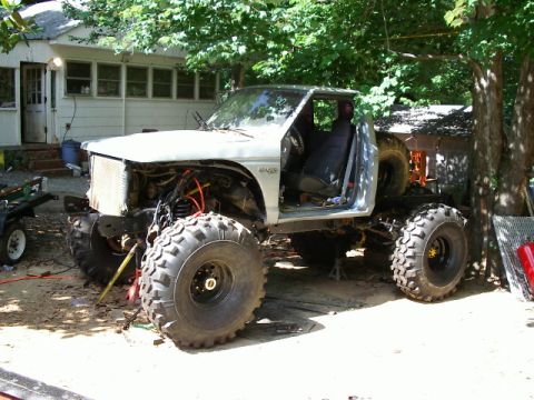 1985 Ford Bronco - A heavily modified pickup truck sits in a yard, undergoing apparent repairs or customization.