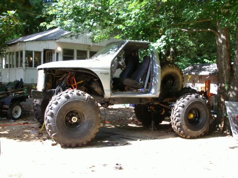 1985 Ford Bronco - This heavily modified truck features massive tires and a lifted suspension, with its front end disassembled.