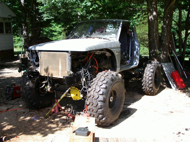 Off-road truck with large tires, missing front clip and engine exposed, on jacks