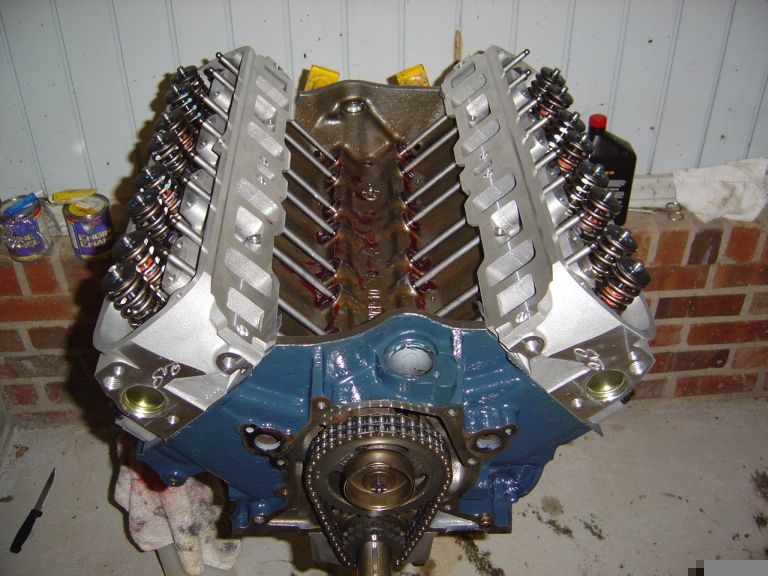 Blue V8 engine on stand with silver heads, exposed pushrods and timing chain