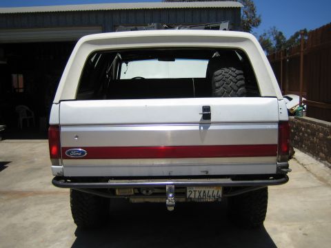 1990 Ford Bronco - Rear of a lifted white Ford full-size SUV with red taillight stripe and California license plate 2TXA444, mud tires and a rear tube bumper.