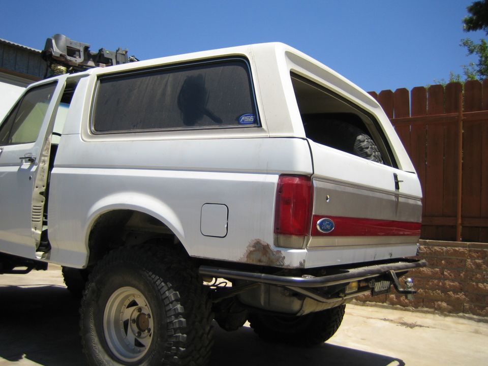 Rear side quarter of a white lifted Ford SUV with red stripe and Ford oval, white wheel and mud tire