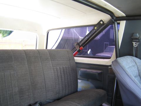 1990 Ford Bronco - Interior view of a cloth rear bench seat with a red-and-black Hi-Lift style jack mounted across the rear side window.