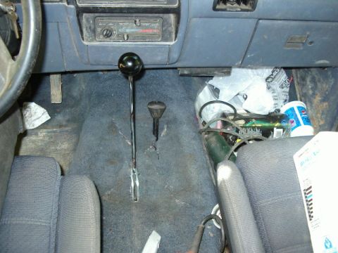 1985 Ford Bronco - The cluttered interior of a vehicle shows a floor shifter and dashboard details.
