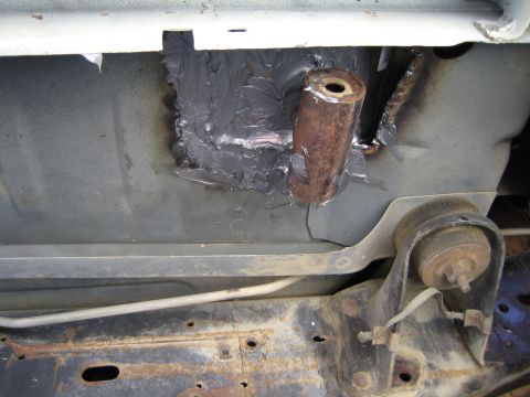 1990 Ford Bronco - Underbody repair detail showing gray seam sealer smeared around a welded copper-toned tube sleeve on a body panel above a suspension mount.