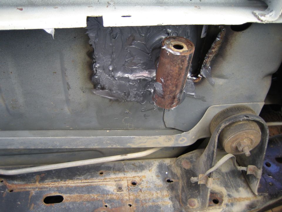 Underbody sheet metal repair with gray seam sealer around a welded copper-colored bushing sleeve