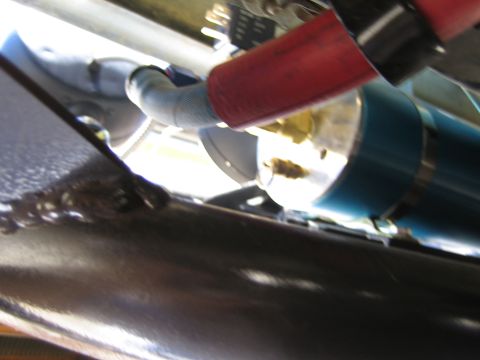 1990 Ford Bronco - Blurry underbody closeup of a red braided hose routed to a blue anodized cylindrical canister beside a polished metal panel.