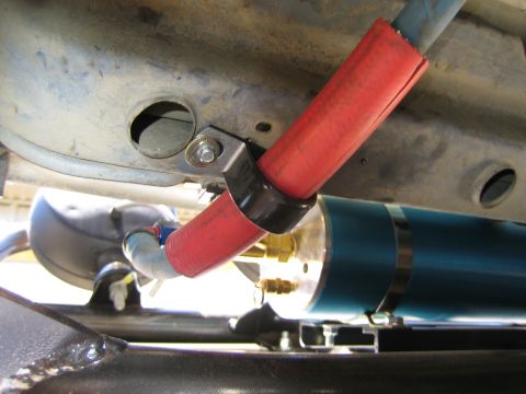 1990 Ford Bronco - Under-vehicle view of a red-sleeved line and blue line joining a fitting on a blue anodized inline fuel filter or pump mounted to the frame.