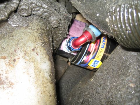 1990 Ford Bronco - Tight closeup of a red anodized fitting and blue line resting on a NAPA Gold filter box wedged between grimy driveline and frame components.