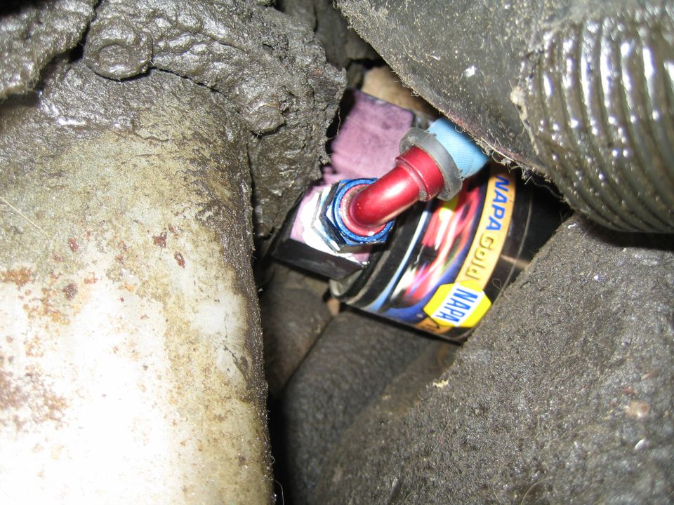 Tight closeup of a red anodized fitting on a NAPA Gold filter box wedged between greasy components