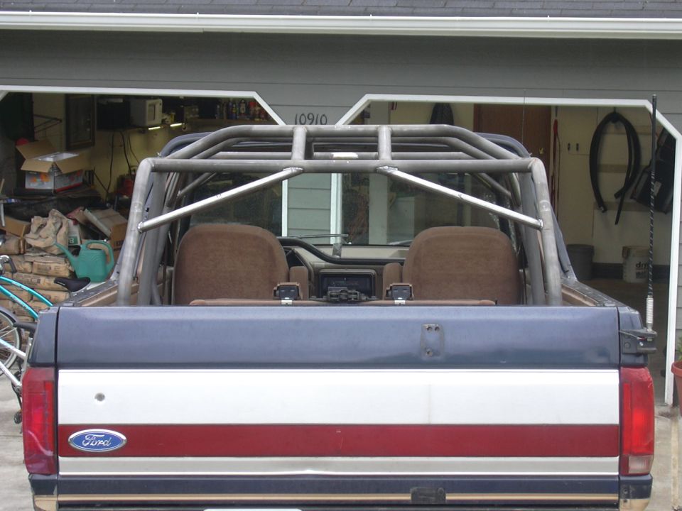 Rear of two-tone Ford truck with custom roll cage, open top, parked in garage