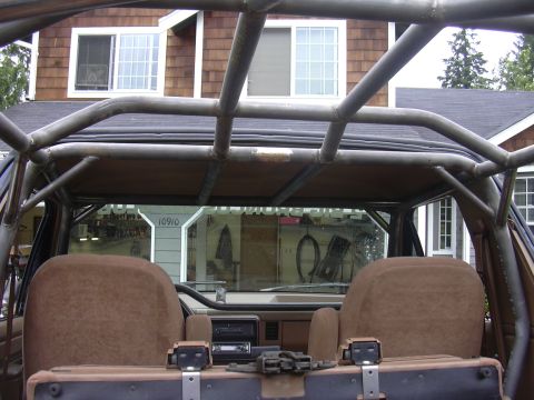 1991 Ford Bronco - Interior rear view of a Ford Bronco showing a custom multi-tube roll cage overhead, two tan cloth front seat backs, a folded rear bench, an…
