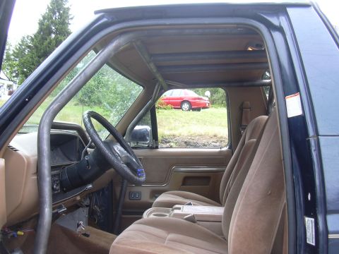 1991 Ford Bronco - Interior view of a truck/SUV cab with tan cloth bench seats, black steering wheel, and a roll bar visible along the roof; the passenger doo…