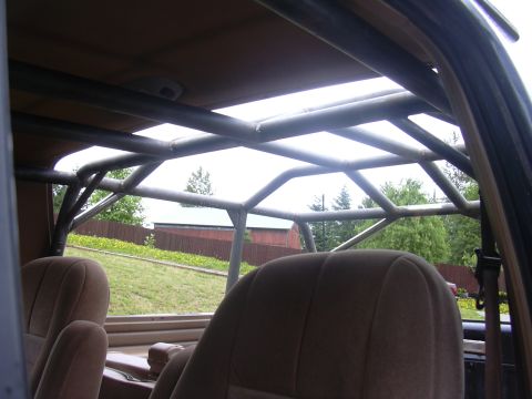 1991 Ford Bronco - Interior view of a Ford Bronco looking up and back at a welded steel roll cage with multiple bars beneath the removable hardtop roof. Tan c…