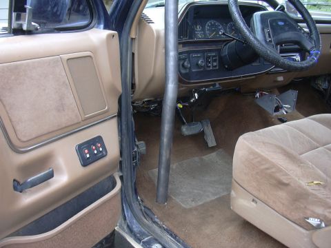 1991 Ford Bronco - Interior view of a Ford truck/SUV shot from the open driver's door, showing tan carpet, door panel, dashboard with round gauges, wrapped st…