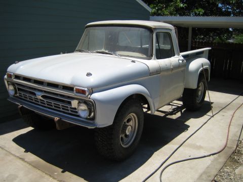 1990 Ford Bronco - Three-quarter view of a vintage white Ford F-series stepside pickup with chrome grille and mud tires, parked on a driveway by a green house.