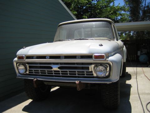 1990 Ford Bronco - Front view of a vintage white Ford pickup showing the FORD-lettered hood, wide chrome grille, round dual headlights and mud tires.