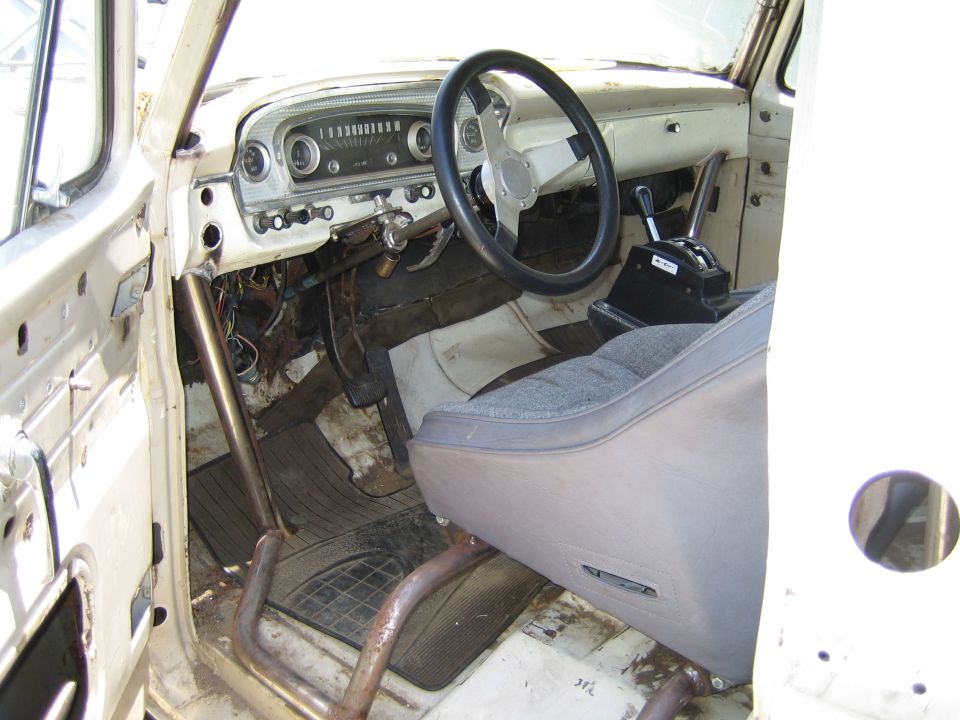Interior of an old white pickup truck showing dashboard, steering wheel and bench seat