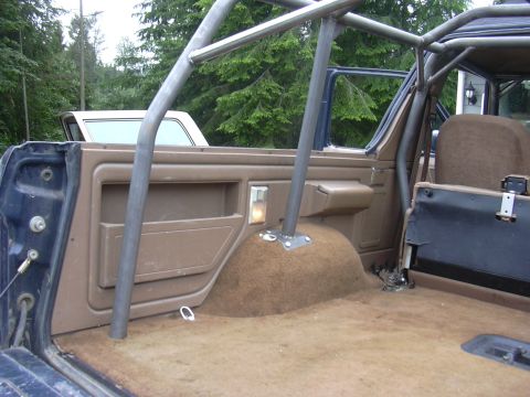 1991 Ford Bronco - Interior rear view of a tan-trimmed Ford Bronco showing the passenger-side door panel, tan carpeting over the wheel well, and a gray tubula…