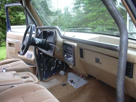 1991 Ford Bronco - Interior of a tan-trimmed Ford truck/SUV viewed from the passenger side, showing the dash mid-disassembly with the radio/climate area expos…