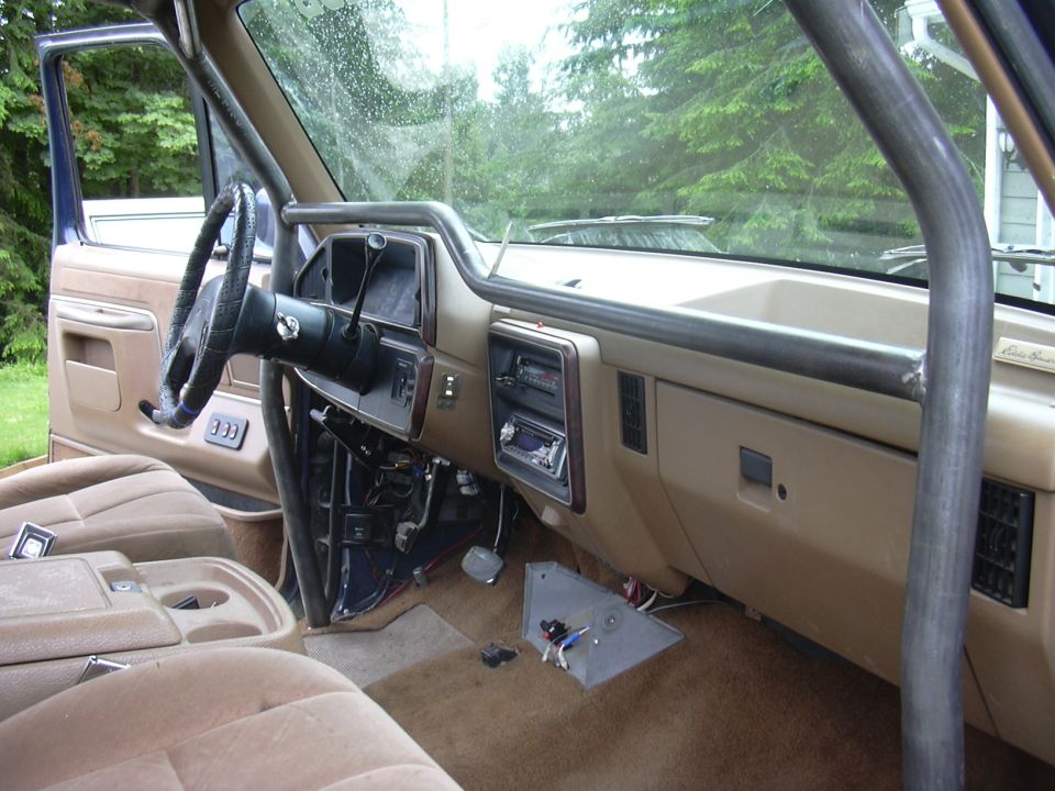 Tan Ford interior with dash apart, roll bar, wiring and metal panel on floor