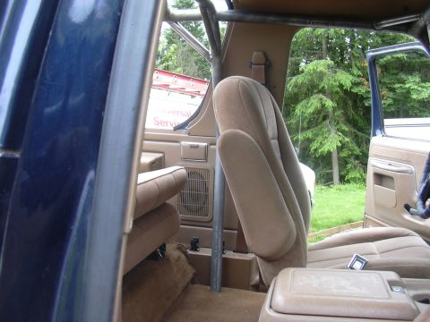 1991 Ford Bronco - Interior view of a tan/beige upholstered SUV looking toward the front passenger seat, showing a roll bar or padded roll cage, rear speaker…