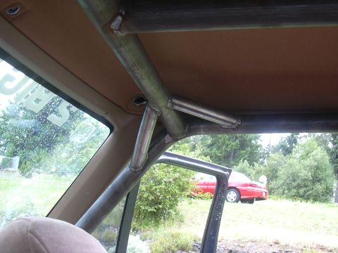1991 Ford Bronco - Interior view looking up at a welded tubular roll cage joint where multiple bare metal tubes meet near the A-pillar and roof, set against a…