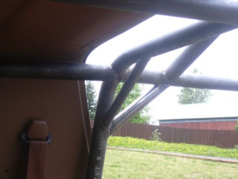 1991 Ford Bronco - Close-up view looking up at a custom welded tubular roll cage or roof frame, with visible weld joints and manufacturer markings printed on…