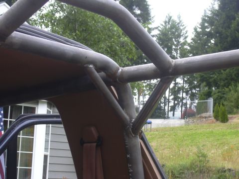 1991 Ford Bronco - Close-up of a bare-steel roll cage node on an open-topped truck, where several welded tubes converge at the B-pillar area above the tan int…
