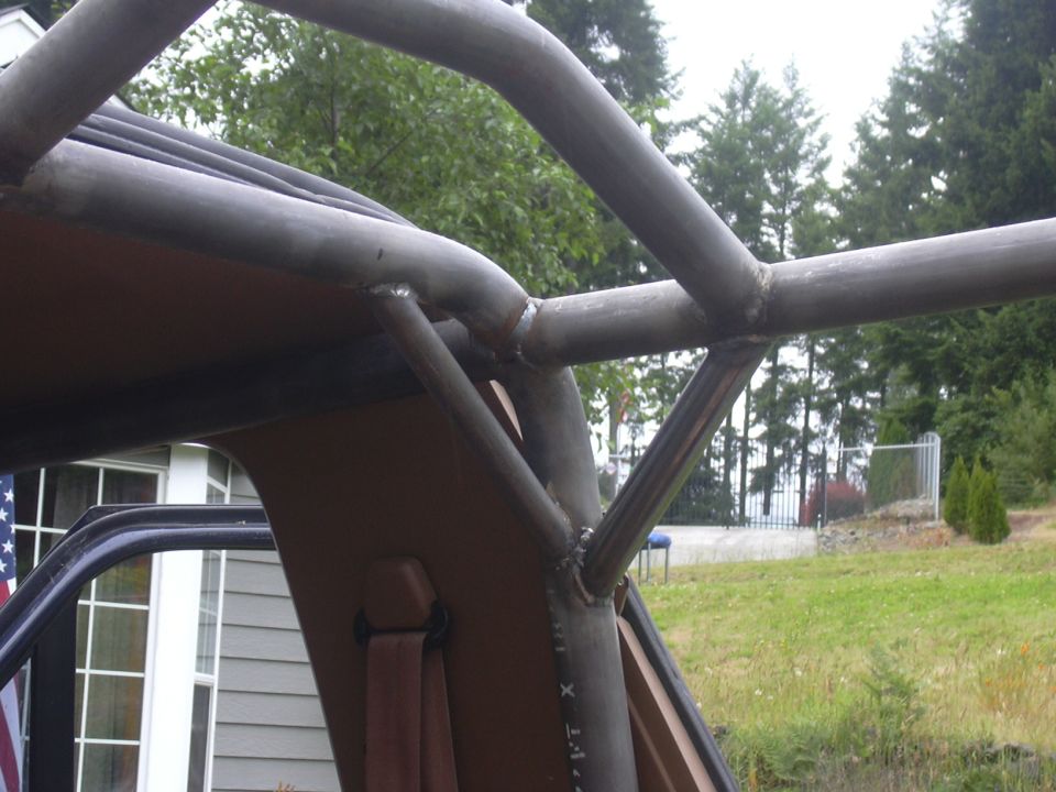 Welded bare-steel roll cage tube junction over the tan interior of an open-top truck