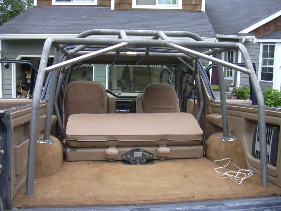 Bronco interior with custom roll cage, tan seats and brown carpet, viewed from open rear hatch
