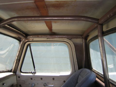 1990 Ford Bronco - Interior view of an old truck cab showing a rusted headliner area, rear window and the top of a cloth seat.