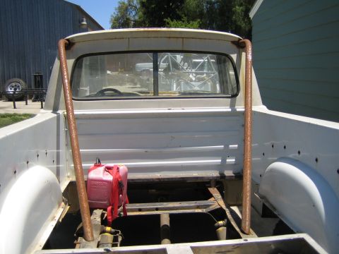 1990 Ford Bronco - Bare white pickup bed with a tall roll bar, exposed frame, and a red plastic fuel container, parked beside a building.