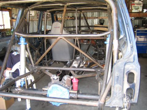 1990 Ford Bronco - vehicle under construction in a garage showing an extensive tube-frame roll cage, single racing seat and exposed chassis.