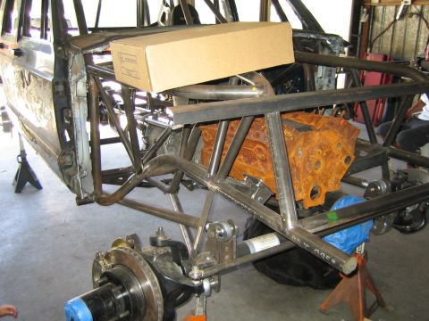 1990 Ford Bronco - Custom tube-frame chassis on jack stands showing front suspension, a brake rotor and a rusty cast engine block during a build.
