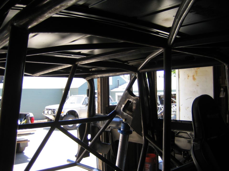Interior of a vehicle with a black tube roll cage looking out toward parked trucks
