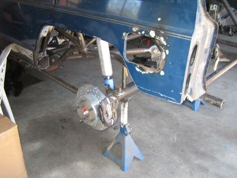 1990 Ford Bronco - blue vehicle on jack stands with bodywork removed, exposing the front coilover suspension and a drilled brake rotor.