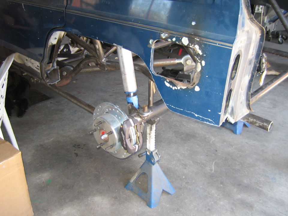 Blue vehicle body on jack stands with exposed front suspension and brake rotor