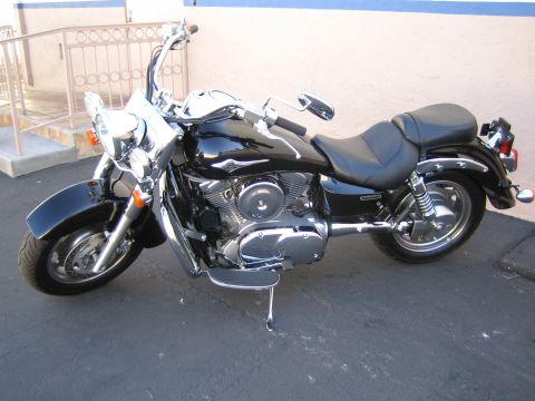 1990 Ford Bronco - Black cruiser motorcycle with chrome engine and dual exhaust parked in profile on pavement beside a metal railing.