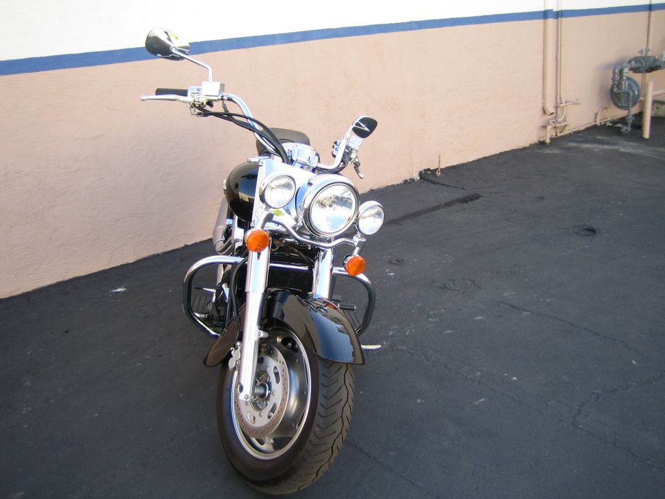 Front view of a black cruiser motorcycle with crash bars parked by a wall