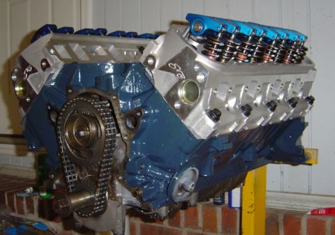 1986 Ford Bronco - A V8 engine assembly, a blue painted block and aluminum cylinder heads, is shown on an engine stand.
