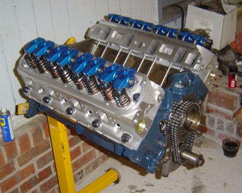 1986 Ford Bronco - Engine block with blue roller rockers and timing chain, mounted on a yellow stand.
