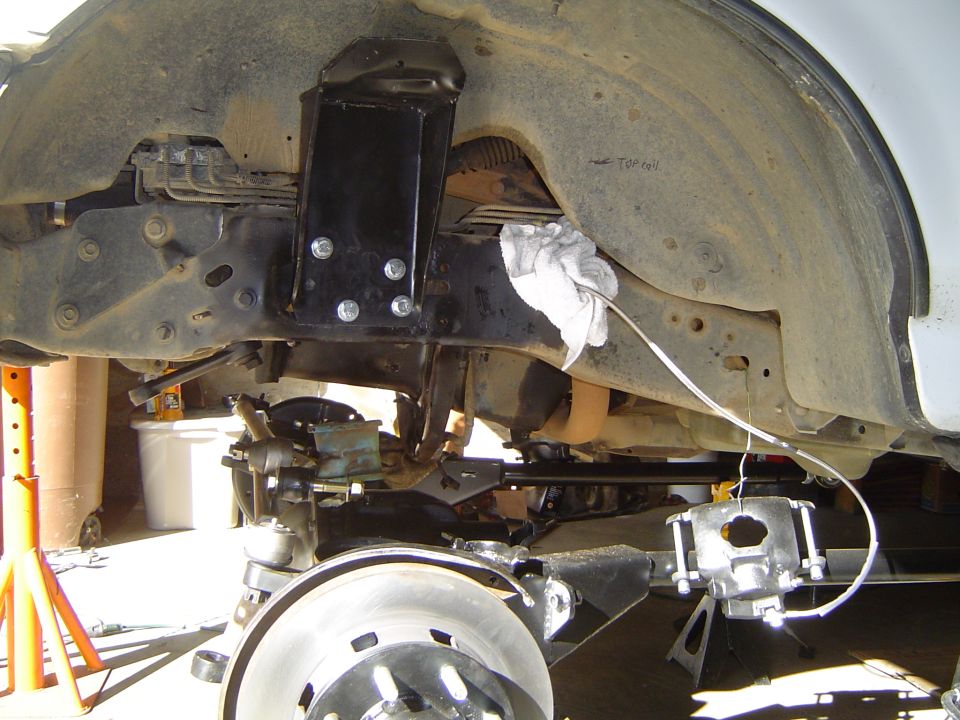 Underside of a white truck showing front differential, skid plate and frame on jack stands
