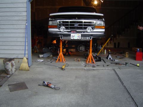 1989 Ford Bronco - A person works on the underside of a Ford truck lifted on jack stands in a garage.
