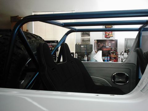 1978 Ford Bronco - The interior of a vehicle shows a roll cage and bucket seats, with a spare tire mounted behind the driver's side.