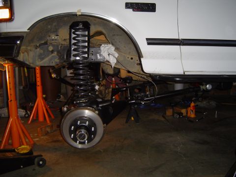 1989 Ford Bronco - Front suspension of a 1989 Ford Bronco undergoing repair, supported by jack stands.